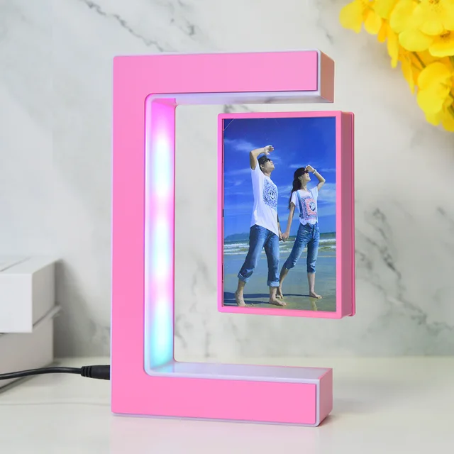 A pink C-shaped LED photo frame with a couple's picture inside. The frame is on a white surface, next to a stack of books and a yellow flower.