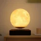 A lunar lamp emitting a warm, yellow light, placed on a wooden surface. The lamp is spherical, resembling the moon, and it appears to be levitating above a dark base. Text above reads "Lunar lamp."