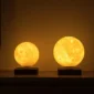 Two illuminated spherical lamps designed to resemble the moon, sitting on square bases against a dark background.