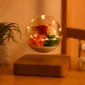 A glass orb with illuminated flowers inside floats above a wooden base, positioned on a wooden surface.