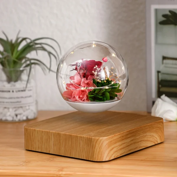 Magnetic Levitating Preserved Flower Rotation Flower Lamp Creative Floating LED Night Light For Home Desk Office Decoration 5 A glass orb with flowers levitating above a wooden base, with a small plant and books in the background.