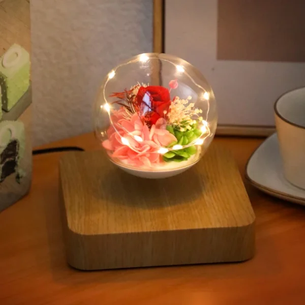 Magnetic Levitating Preserved Flower Rotation Flower Lamp Creative Floating LED Night Light For Home Desk Office Decoration – Light Color 7 A levitating glass orb with flowers and lights, set on a wooden base, next to a teacup on a table.
